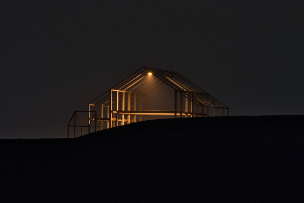 Das bei Dunkelheit beleuchtete Hallenhaus, eine aus Stahl bestehende Hausähnliche Skulptur auf der Halde Norddeutschland