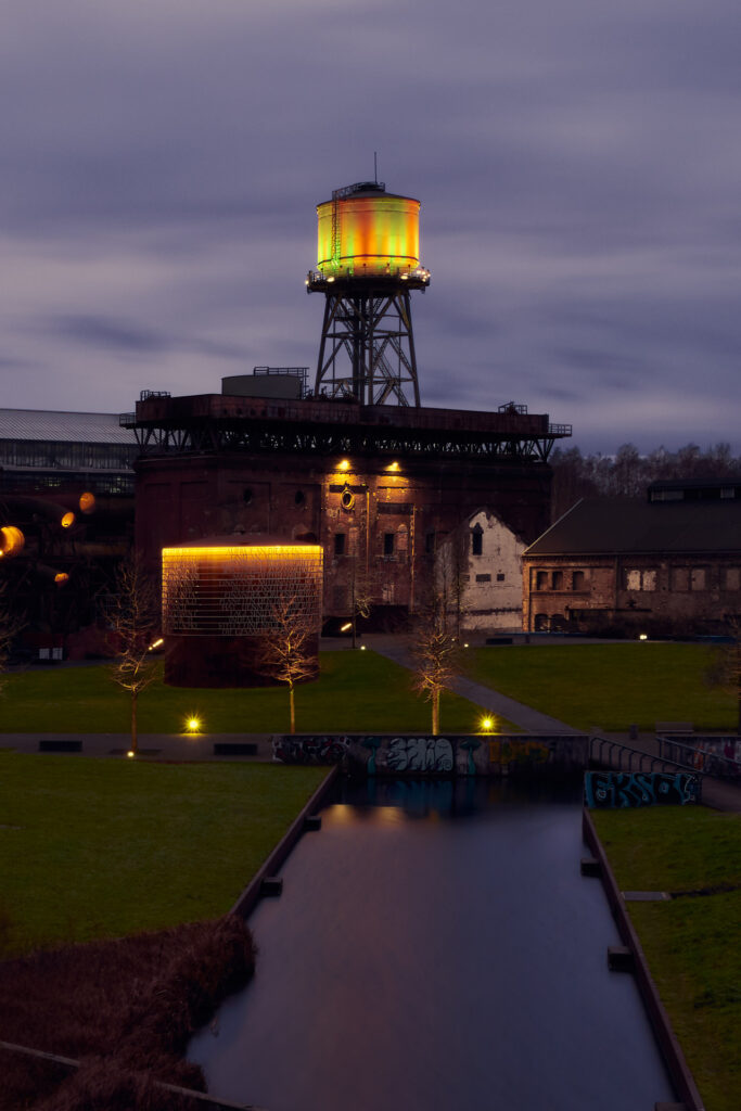 Der Bochumer Westpark in den Abendstunden, der Wasserturm, sowie ein Stahlkunstwerk sind beleuchtet.